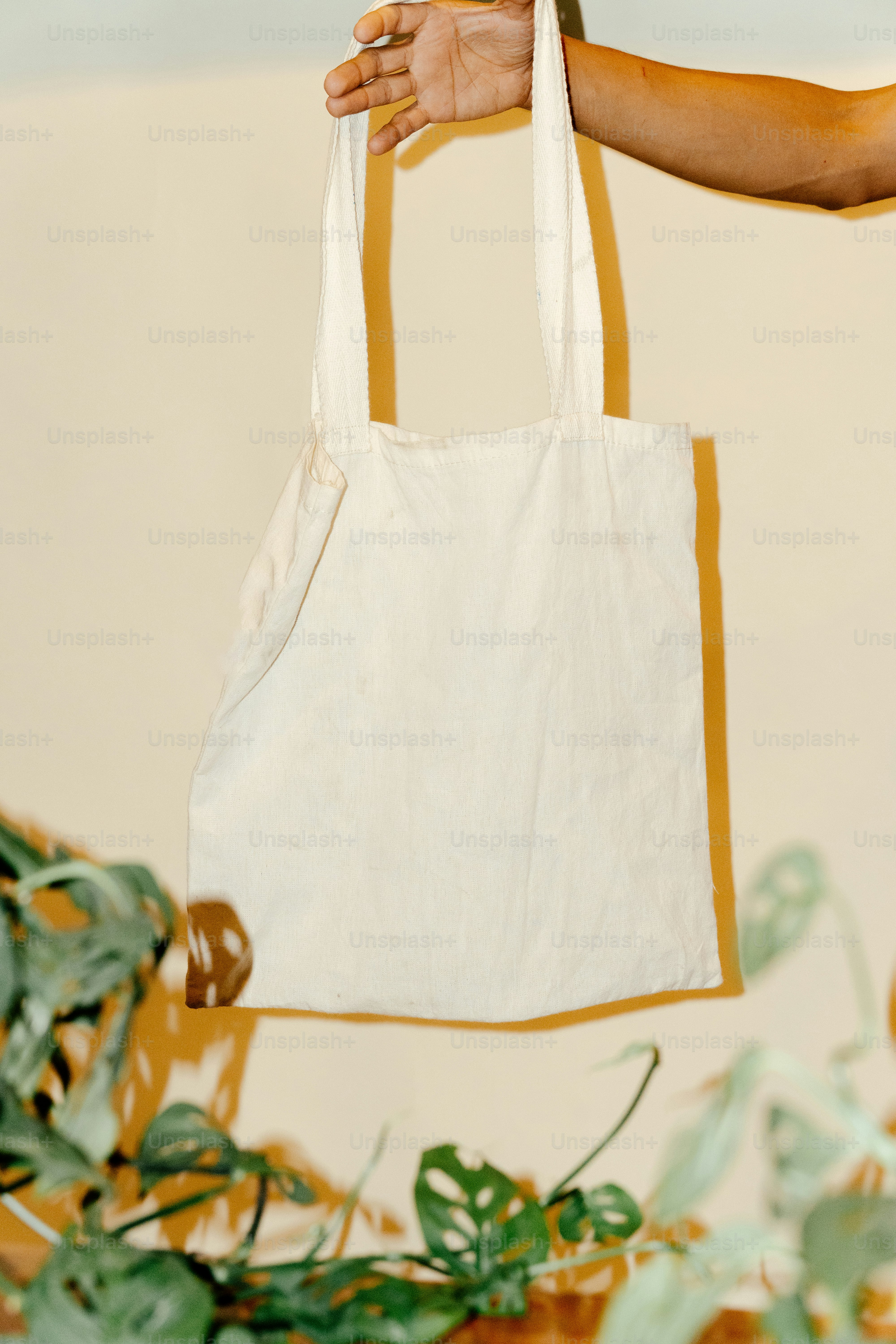 A hand holds up a white tote bag.